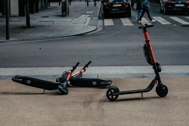 Two e-scooters are on the sidewalk.